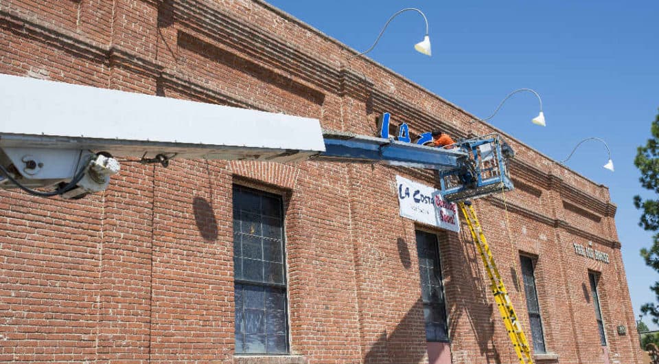 small crane carrying worker to install sign on brick building
